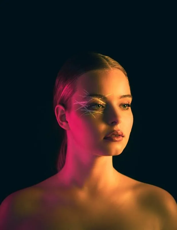 Portrait of Nina Schwarz lit in pink and gold with graphic eye make-up