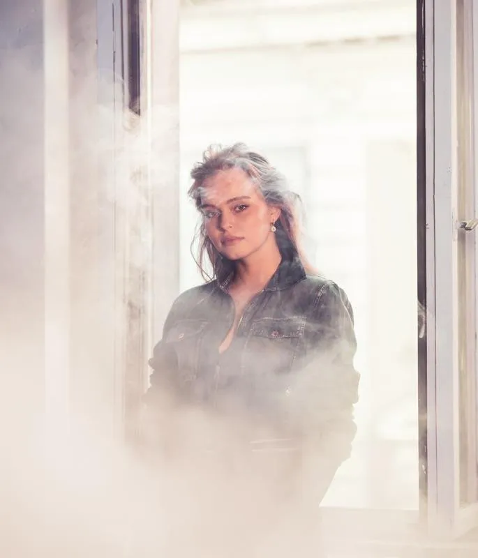 Nina Schwarz in a dark jacket by a window, surrounded by haze