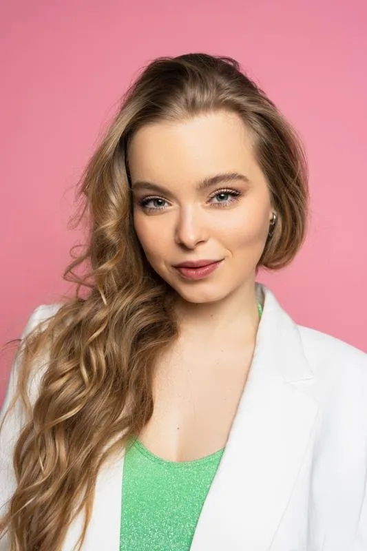 Portrait of Nina Schwarz in a white blazer against a pink backdrop