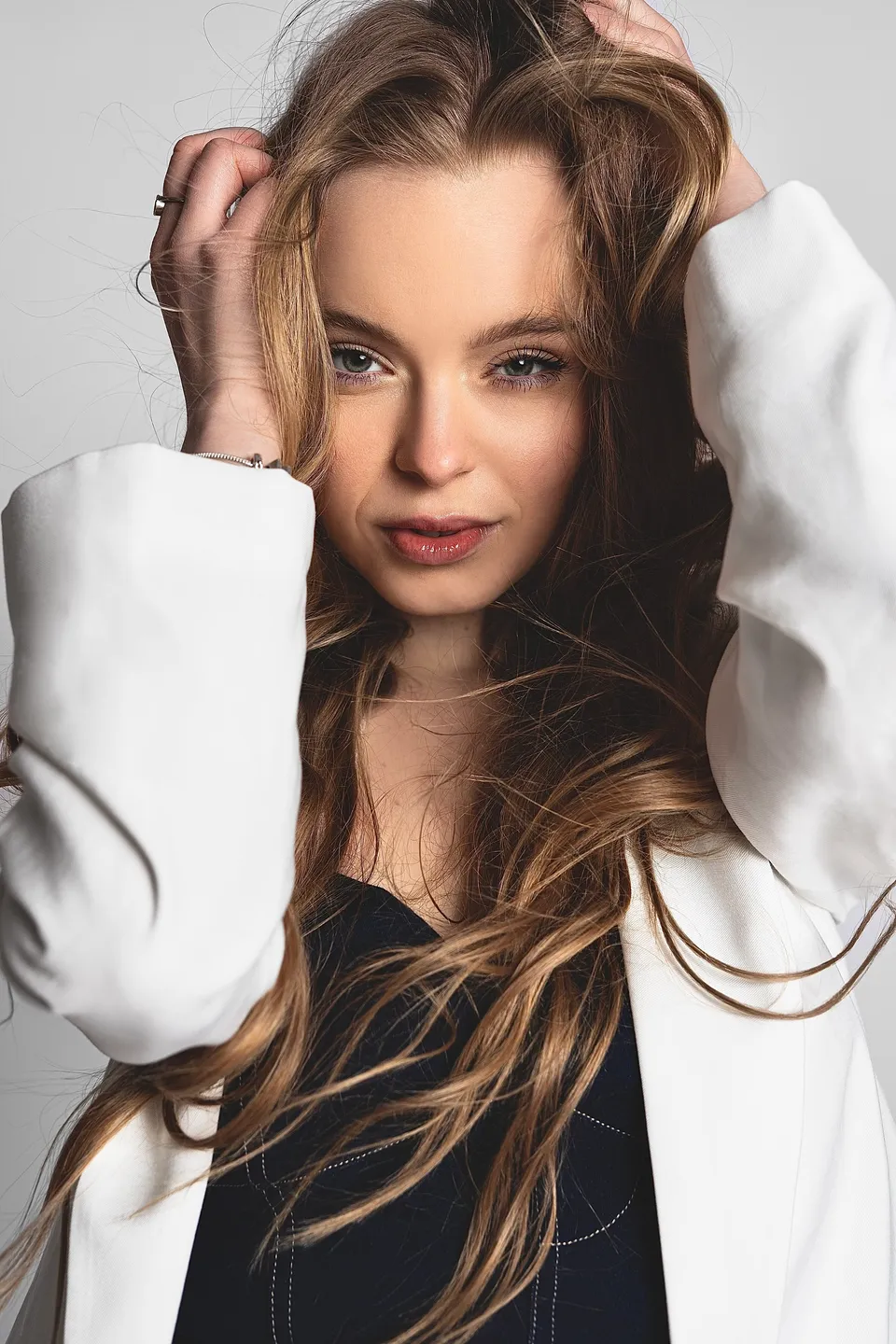 Close-up of Nina Schwarz in a white blazer with her hands in her hair